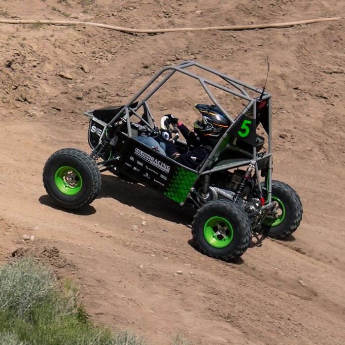 A driver drives the Baja car up a steep dirt hill.