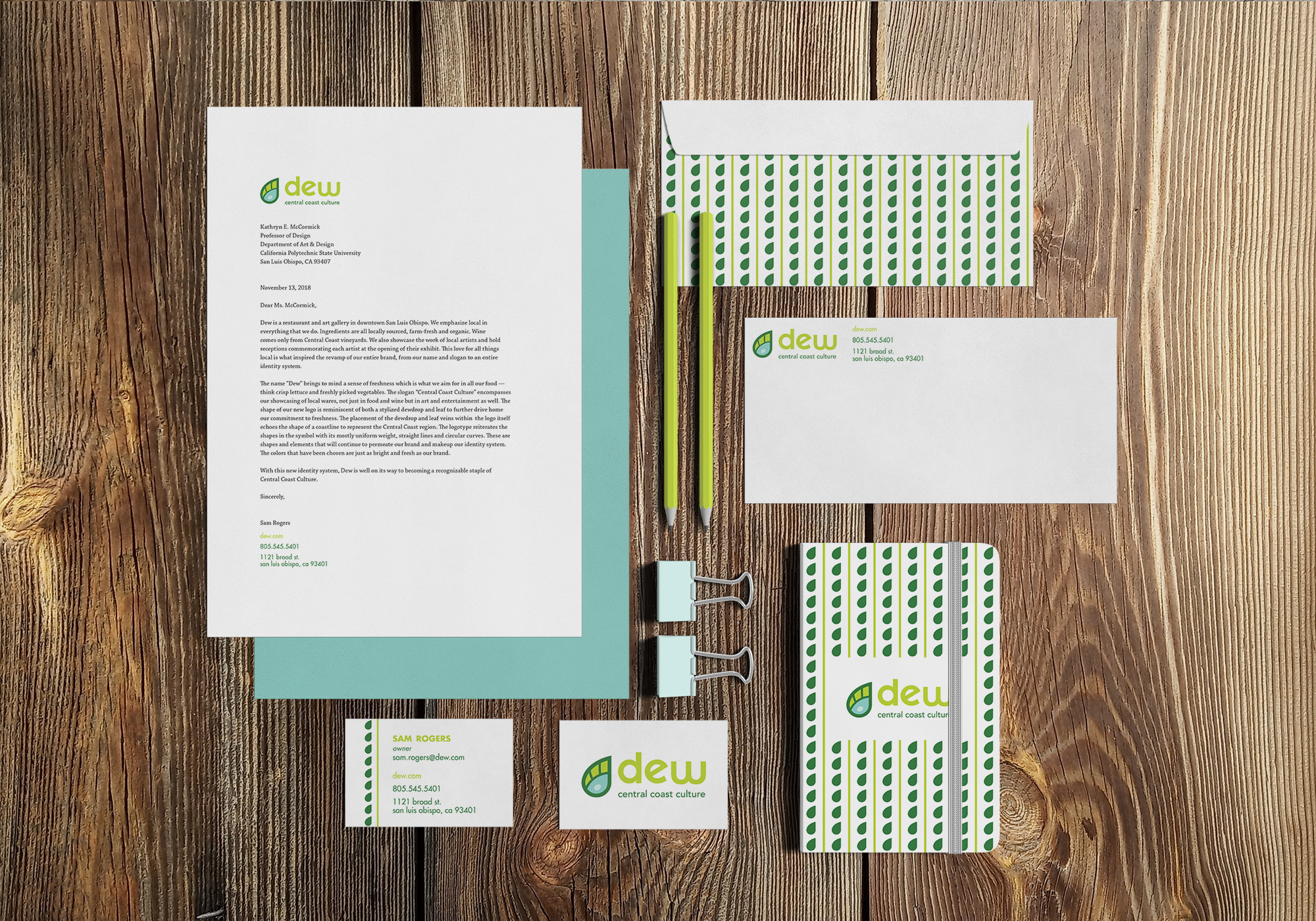 The front and back of an envelope, two business cards, a notebook, and a formal letter with Dew branding and company information on a wooden tabletop.