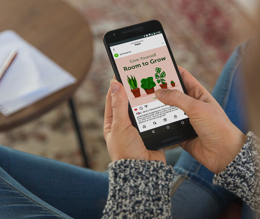 A woman looking at a Grove instagram post. The post shows an illustration of four potted plants and the words “Give yourself room to grow” over a pink background.