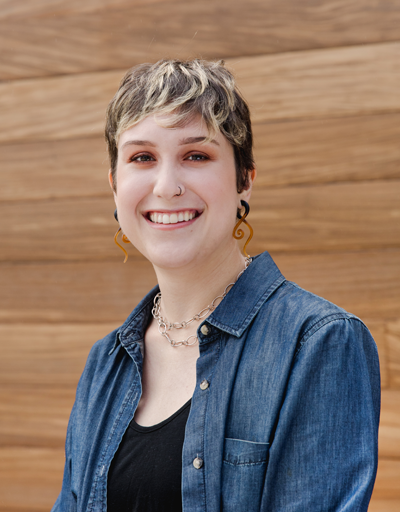 Headshot of Sam Rogers smiling against a wood-panelled background.